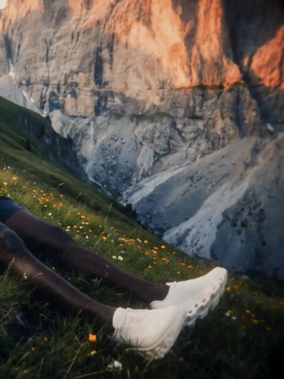 Runner lying in flowering grass, white shoes in the foreground, sunlit cliffs above